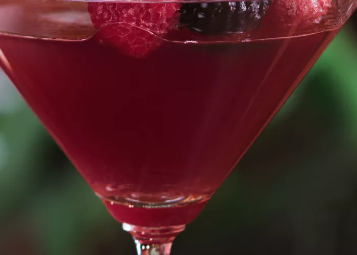 A cocktail glass of Pineapple Razztini, garnished with a pineapple slice and raspberry on a cocktail pick.