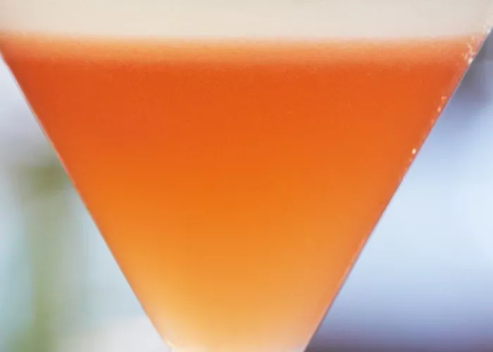 A martini glass of Pink Pineapple-Tini garnished with a cherry and pinapple sticks on a cocktail pick.