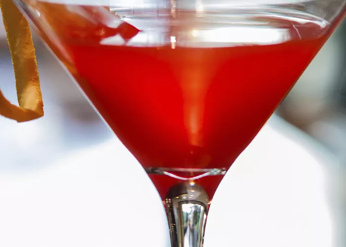 A martini glass of Red Greyhound Pinn-Tini garnished with an orange slice and a straw in it.