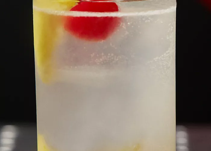 A glass of Juan Collins garnished with lemon peel, Cherry and ice cubes