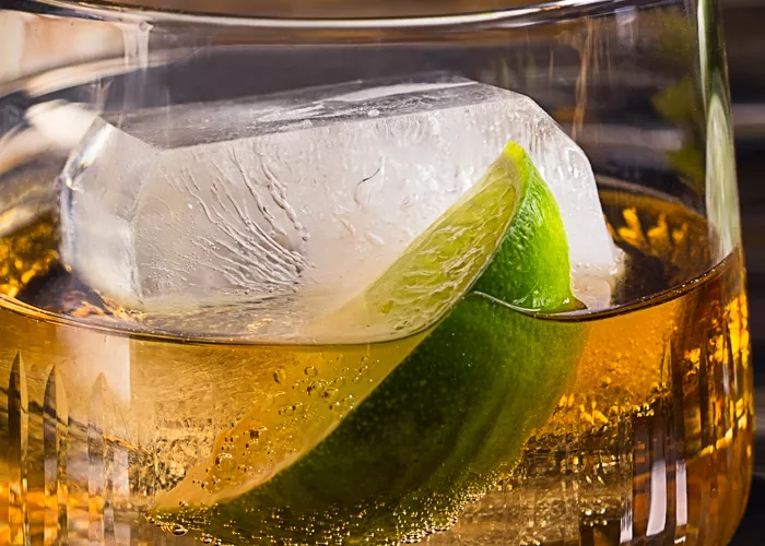 a glass of C.C.® & Ginger garnished with ice and lime slice on coaster