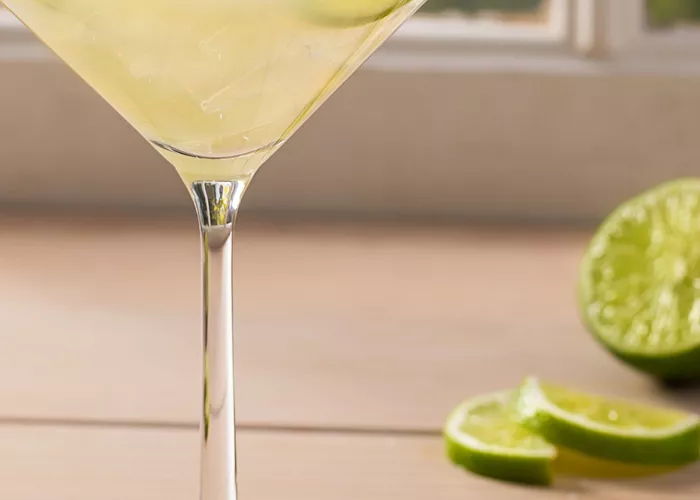 A glass of Sauza® Classic Margarita garnished with lemon slices and salt alongside few lime slices