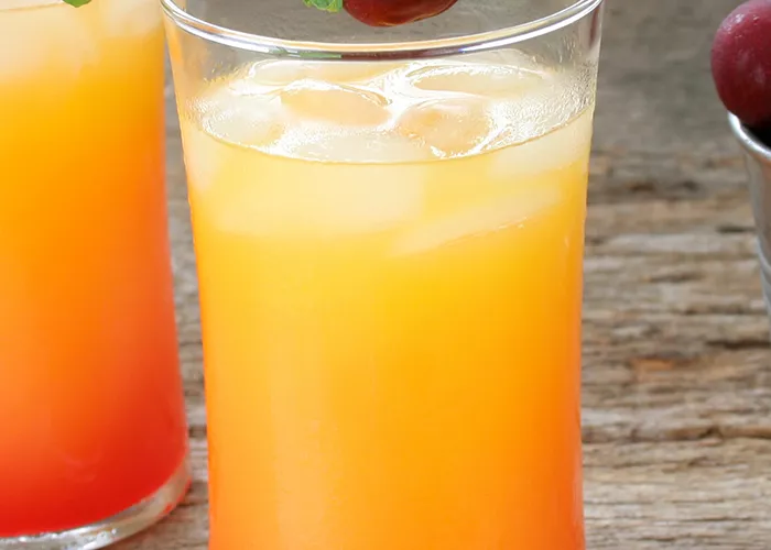 Two glasses of Cruzan® 9 Punch garnished with cherry and mint leaves alongside bucket of cherries