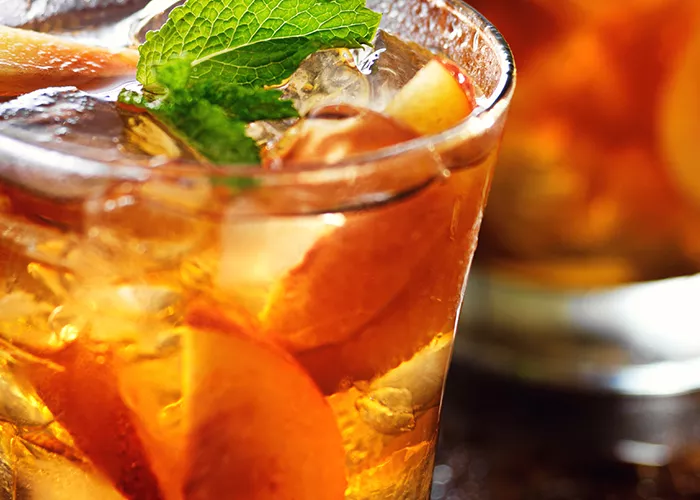 Glasses of Peach Mojito garnished with a mint sprig and a peach slice with some oranges spread alongside.