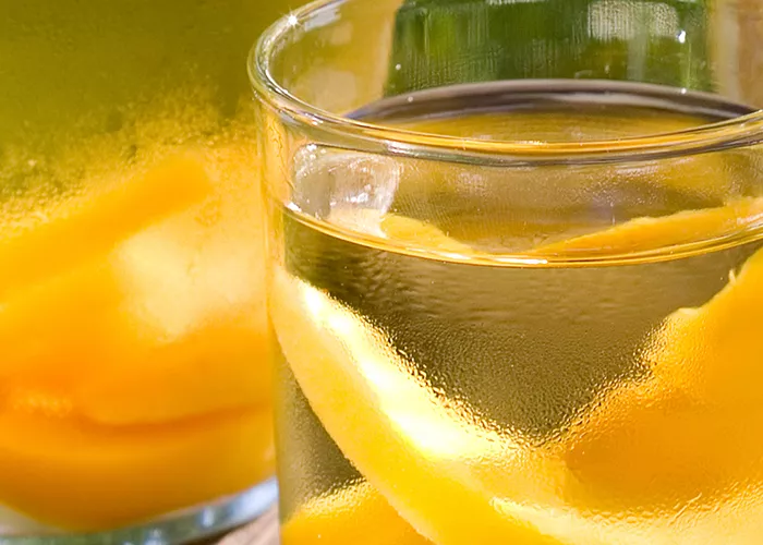 A glass of Cruzan® Peach Sangria, garnished with lime slices, sits next to a jar filled with the same sangria.