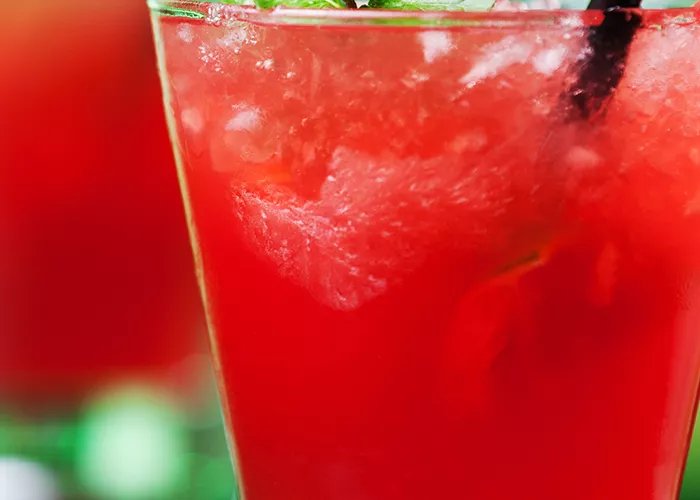 Glass of Berry Burst with straws garnished with mint leaves on steel coaster