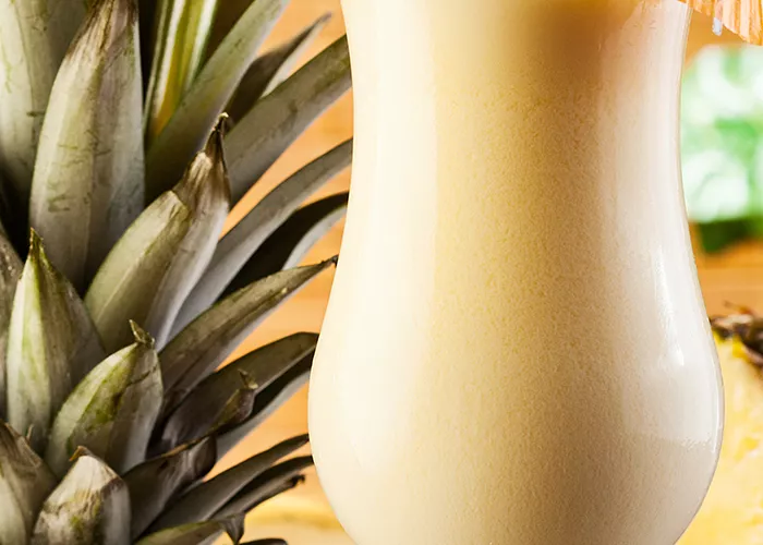 A glass of Amaretto Pina Colada, decorated with a cocktail umbrella on the rim of the glass and a straws