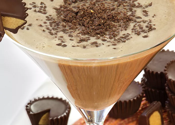 Glass of Peanut Butter Cup Martini garnished with Peanut Butter Cup alongside few Peanut Butter Cups