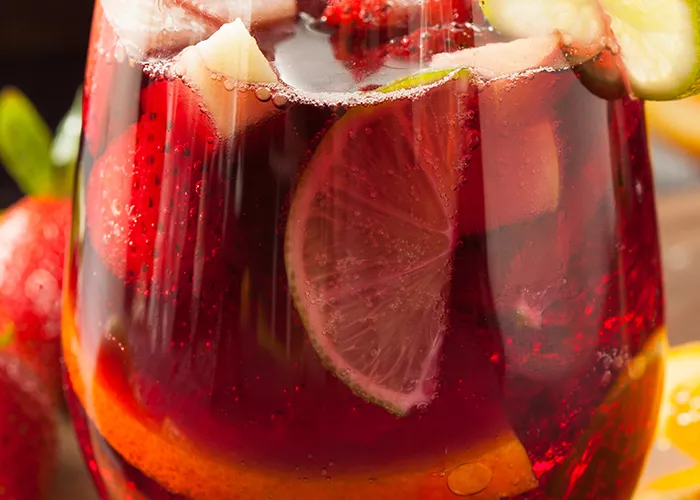 1.A glass of Razzmatazz® Sangria garnished with  chopped fruits and a lemon slice on a rim along side few strawberries and orange slices