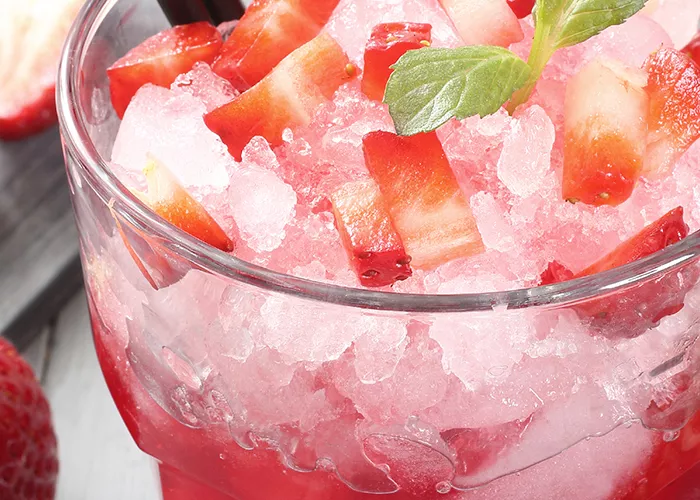 Glass of strawberry Margarita garnished with crushed ice, strawsberry pieces, mint leaves and straws