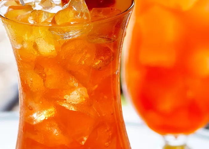 A glass of Watermelon Mai Tai, garnished with ice cubes, a cherry, orange and  pineapple slice on the rim of the glass, and a cocktail umbrella