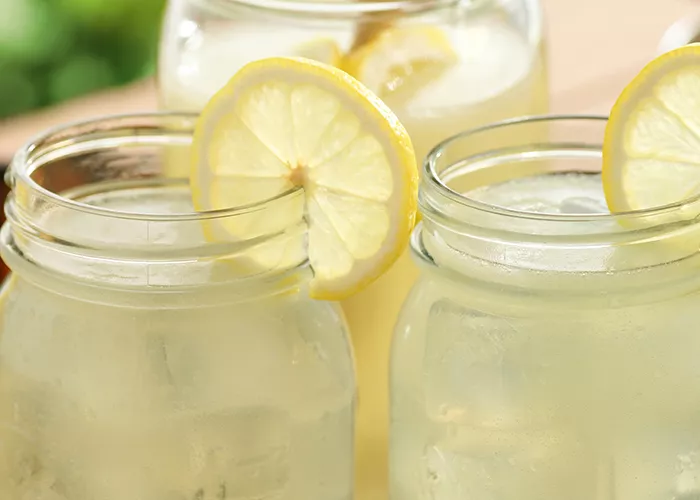Two jars of Jim Beam® Lemonade garnished with lemon slice in a basket alongside few lemons