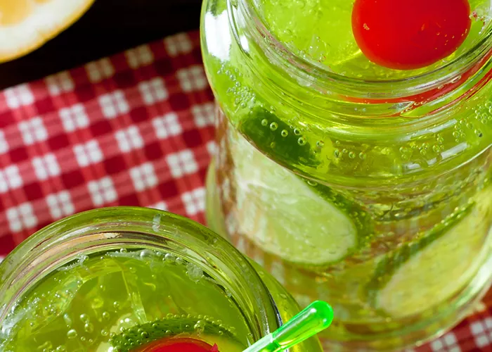 Two Jar of Midori® and Ginger garnished with a cherry on a napkeen alongside  a half orange.