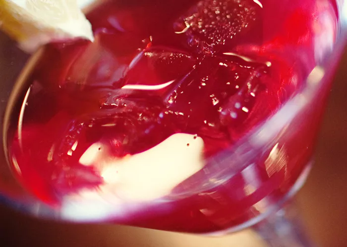 A martini glass of Grape Cosmo, garnished with an orange slice.