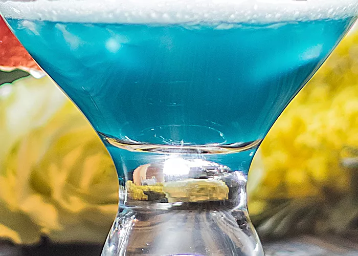 A cocktail glass of Sauza® Blue garnished with blood orange slice and cherry with crushed sugar rim.