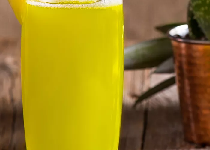Glass of Midori® Cactus Juice with a  straw, garnished with a pineapple wedge on a green napkin, alongside a cactus plant.