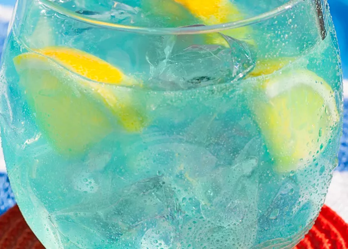 Glass of Pool Party Punch with ice and lemon slices on red coaster