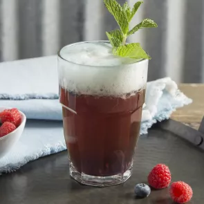 glass of Berry Good Shandy garnished with mint leaves alongside some berries