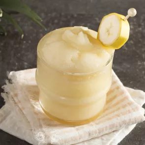 Glass of Banana ‘Nana Daiquiri garnished with banana slice on white cloth