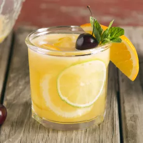 Glass of Sparkling Cherry Sangria garnished with orange wedge, lime slices, mint leaves and cherry