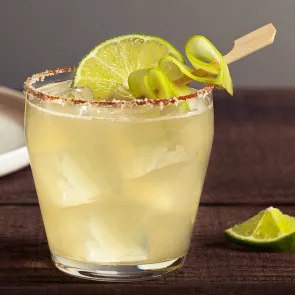 Glass of Spicy Cucumber Margarita garnished with thin cucumber slice and lime slice alongside lemon wedge