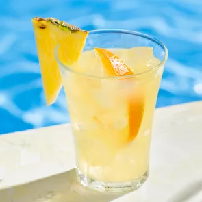 A glass of Endless Summer Punch garnished with ice cubes, an orange slice, and a pineapple slice on the rim