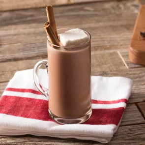 a mug of fireside coco  on a napkin garnished with marshmallows and cinnamon stick