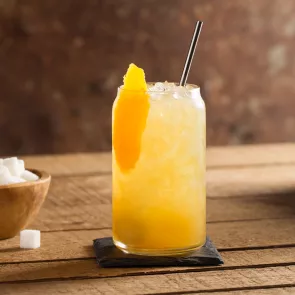 Glass of The Rider with ice and straws garnished with orange peel on black coaster alongside a bowl of suger cubes