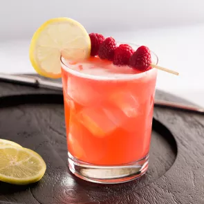 Glass of Ruby Sparkler garnished with lemon slice and raspberries alongside lemon slice 