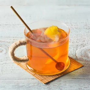 Cup of Hot Toddy garnished with lemon peel with a wooden spoon