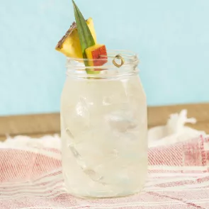  Cruzan® Confusion served in a glass with pineapple, pineapple leaves, and mango on a table with a cloth.