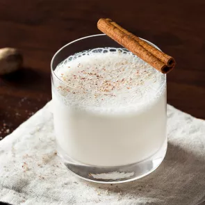 Glass of Bourbon Milk Punch on a napkin, garnished with a cinnamon stick.