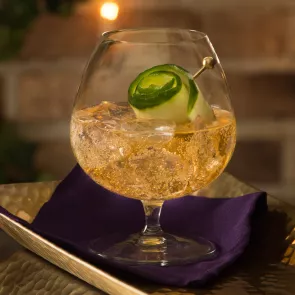 Glass of Cognac Summit garnished with cucumber peel and crushed ice, placed on a napkin on a tray