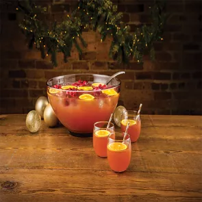 Three glasses of Holly Jolly Punch garnished with orange slice and straws alongside pot of Holly Jolly Punch 