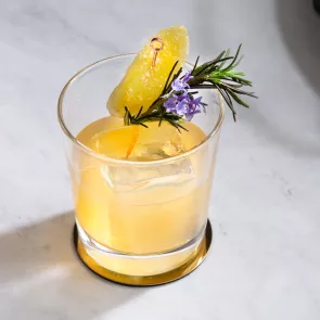 A glass of Ginger Buck garnished with Sprig of Rosemary and Candied Ginger