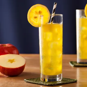 Two glasses of Midori® Cider with strawss on coasters, garnished with lemon wheels. Nearby, there is one and half apple.