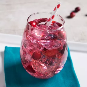 A glass of flirty fizz cocktail with ice and a straw on blue coaster