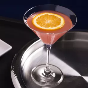 Glass of El Bombín garnished with an orange slice on a steel tray.