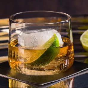 a glass of C.C.® & Ginger garnished with ice and lime slice on coaster