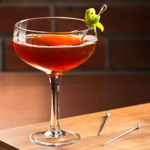 Glass of Jim Beam Orleans garnished with a lime twist, alongside two swizzle sticks.
