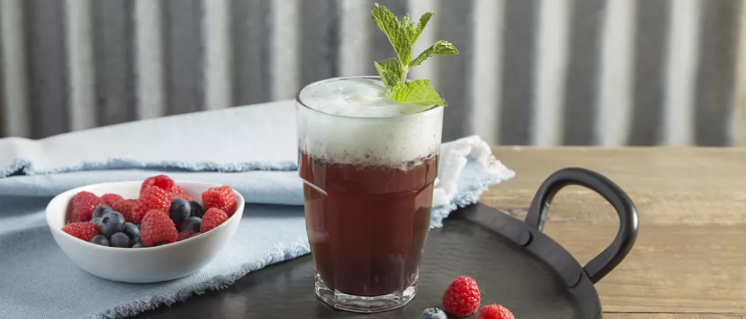 glass of Berry Good Shandy garnished with mint leaves alongside bowl of berries