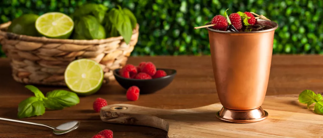 Glass of Berry Moscow Mule garnished with raspberries and mint leaves on wooden board