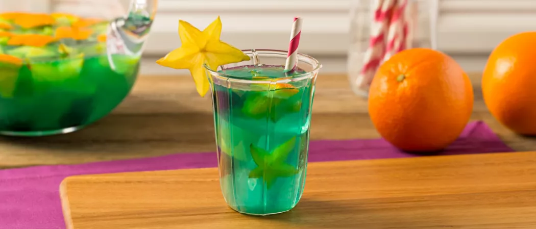 Glass of Blue Lagoon Sangria garnished with starfruit slice on wooden tray alongside orange
