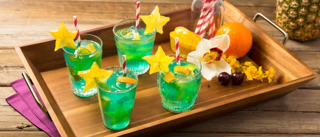 Four glasses of Blue Lagoon Sangria garnished with starfruit on a tray alongside starfruit, orange and two cherries