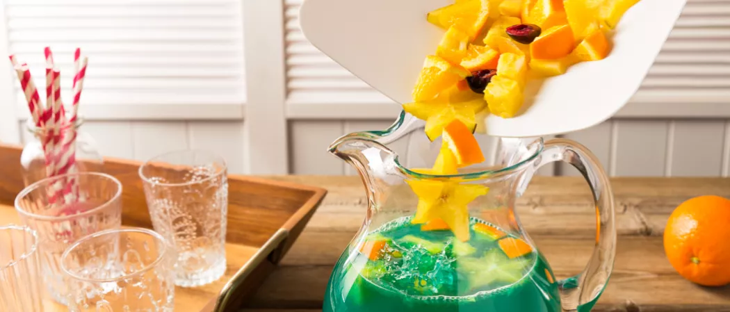 a Person adding starfruit and orange pieces into jar of Blue Lagoon Sangria