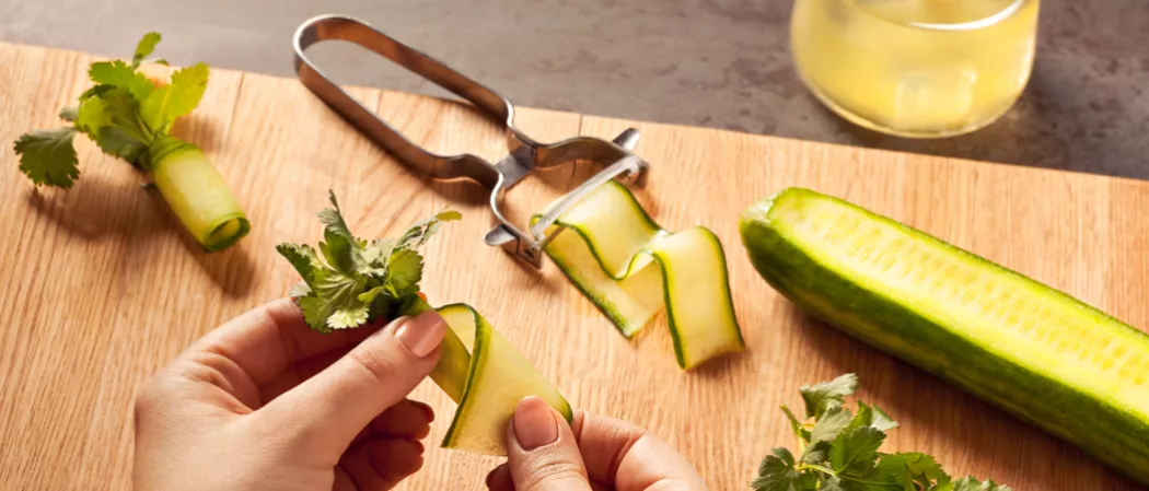 Person wrapping sprig of cilantro with a thin slice of fresh cucumber 