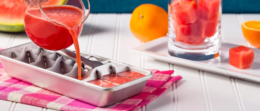 Person pouring watermelon puree into ice tray