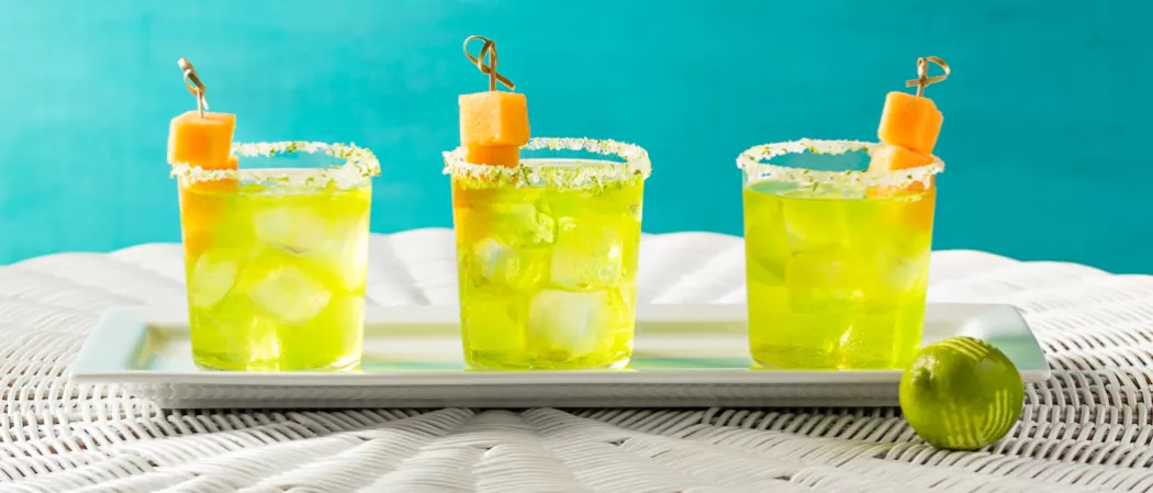 Three glasses of Cucumber Melon Margarita garnished with melon cubes on white tray