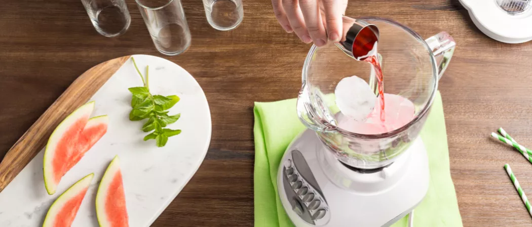 Person Downward Facing Daiquiri into blender alongside wodden board with watermelon slices and mint leaves
