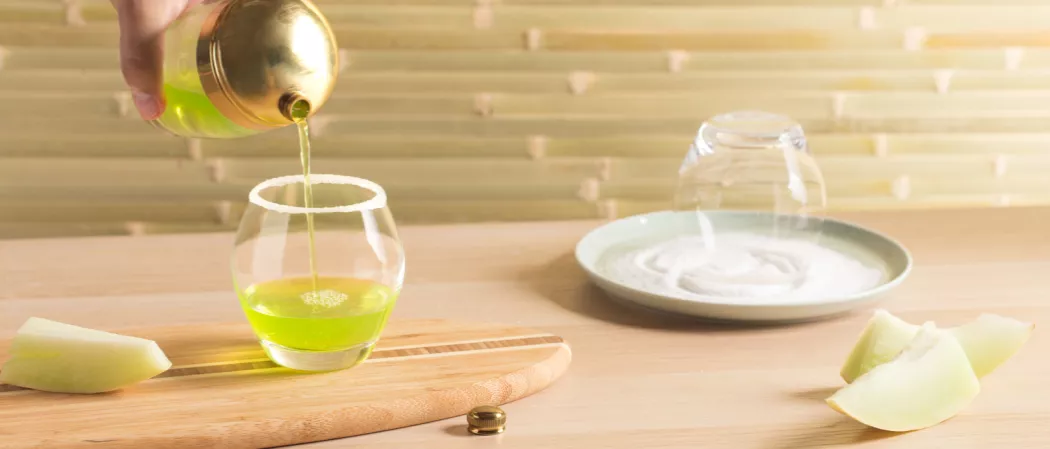 A person pouring emerald daiquiri in a glass.